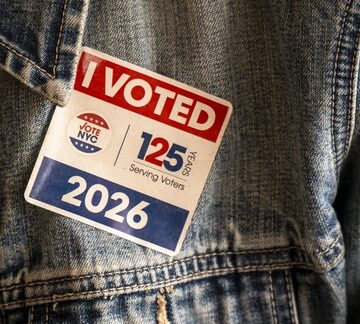 A sticker with the "Vote NYC" logo, the text "125 Years Serving Voters," and the year 2026 pasted on the front of a denim jacket. A sticker with the "Vote NYC" logo, the text "125 Years Serving Voters," and the year 2026 pasted on the front of a denim jacket.
