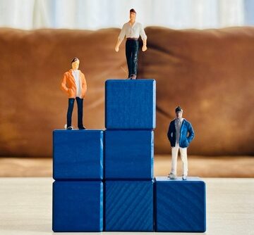 Miniature human figurines arranged on blue blocks to represent a hierarchy or social class pyramid. Miniature human figurines arranged on blue blocks to represent a hierarchy or social class pyramid.