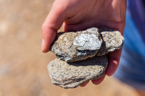 A person holding samples of specular hematite or a similar micaceous mineral, characterized by its shiny, flaky, silver-grey appearance.