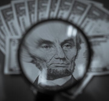 Close-up view of a magnifying glass focused on the portrait of Abraham Lincoln on a U.S. five-dollar bill. Close-up view of a magnifying glass focused on the portrait of Abraham Lincoln on a U.S. five-dollar bill.