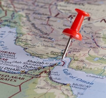 A red pushpin on a map is placed directly on the Strait of Hormuz, a strategically crucial waterway connecting the Persian Gulf to the Gulf of Oman and the Arabian Sea.