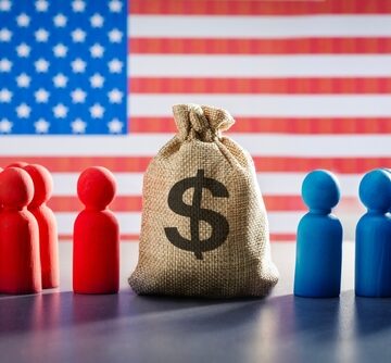 Red and blue figures representing political parties facing a money bag with the U.S. flag in the background. Red and blue figures representing political parties facing a money bag with the U.S. flag in the background.