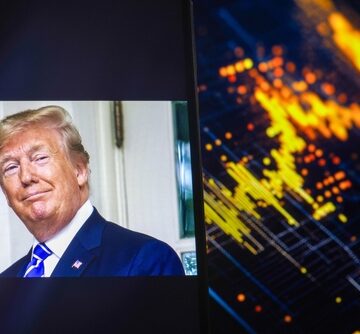 A smartphone screen showing Donald Trump positioned next to a glowing stock market data visualization on a computer monitor. A smartphone screen showing Donald Trump positioned next to a glowing stock market data visualization on a computer monitor.