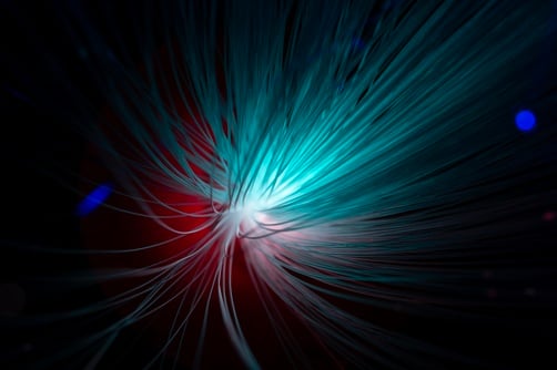 A close-up of fiber optic strands emitting a bright blue and white light burst against a dark background.