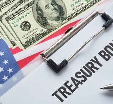 A clipboard labeled "Treasury Bonds" sits atop a U.S. flag and U.S. currency.