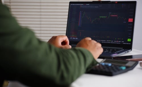 A person analyzing a financial candlestick chart on a laptop screen, likely tracking financial markets like stocks, forex, or cryptocurrency.