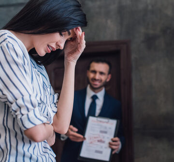 A distressed woman in a striped shirt holds her head while her unhappy husband points to bills. A distressed woman in a striped shirt holds her head while her unhappy husband points to bills.