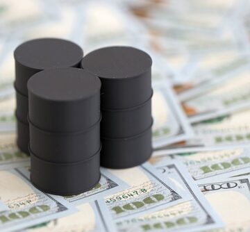 Miniature barrels of oil on a tabletop covered with U.S. $100 dollar bills.