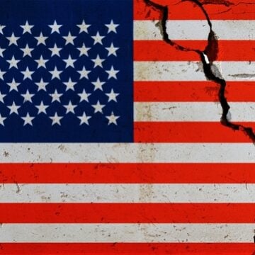 An American flag with a large, jagged crack running through the stripes on the right side.