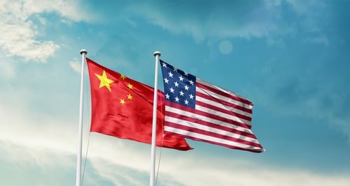 The national flags of the People's Republic of China (left) and the United States of America (right) flying side-by-side against a blue sky.