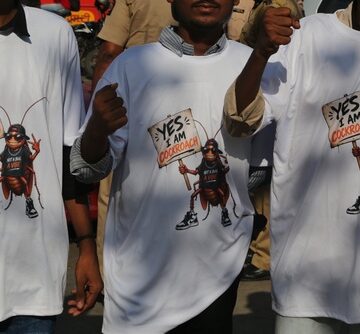 White cotton t-shirts featuring a graphic of a cartoon cockroach holding a sign that reads "YES I AM COCKROACH" in Mumbai, India. White cotton t-shirts featuring a graphic of a cartoon cockroach holding a sign that reads "YES I AM COCKROACH" in Mumbai, India.