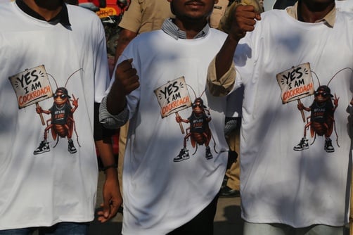White cotton t-shirts featuring a graphic of a cartoon cockroach holding a sign that reads "YES I AM COCKROACH" in Mumbai, India.