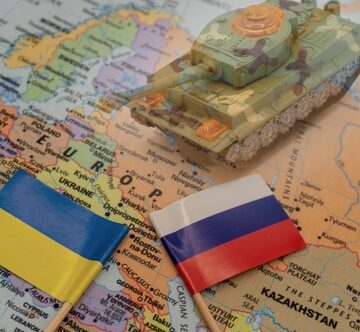 The Ukraine and the Russian Federation flags placed next to a toy tank on a map of Europe. The Ukraine and the Russian Federation flags placed next to a toy tank on a map of Europe.