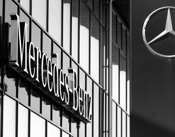 A modern Mercedes dealership facade with large glass panels featuring the iconic silver three-pointed star logo on a black background. A modern Mercedes dealership facade with large glass panels featuring the iconic silver three-pointed star logo on a black background.