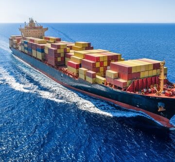 A fully loaded container ship navigating through the open blue sea, leaving a white wake in the water behind it. A fully loaded container ship navigating through the open blue sea, leaving a white wake in the water behind it.