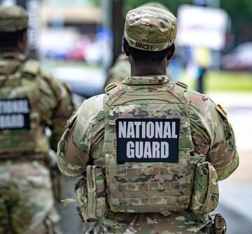 U.S. National Guard members wearing operational camouflage uniforms and tactical vests with prominent "National Guard" identification patches during domestic urban patrols.