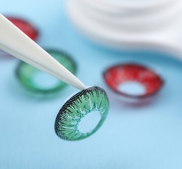 Tweezers holding colored contact lenses, often used for cosmetic purposes or costumes, but classified as medical devices and obtained with a prescription to ensure proper fit.