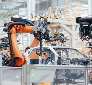 Orange industrial robotic arms work on a vehicle chassis along an automated assembly line in a modern automotive manufacturing plant.