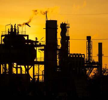 The silhouette of an industrial refinery petrochemical plant highlighted by a yellow-orange sunset. The silhouette of an industrial refinery petrochemical plant highlighted by a yellow-orange sunset.