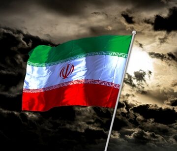 The Iranian national flag flying against a dark, cloudy sky. The Iranian national flag flying against a dark, cloudy sky.