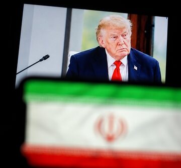 Donald Trump at a podium with a blurred image of the flag of Iran in the foreground.