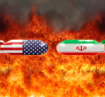 A digital illustration depicting two opposing missile or bomb shapes draped in the national flags of the United States and Iran, set against a fiery background.