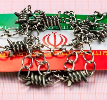 Image of a metal chain and barbed wire wrapped over the national flag of Iran.