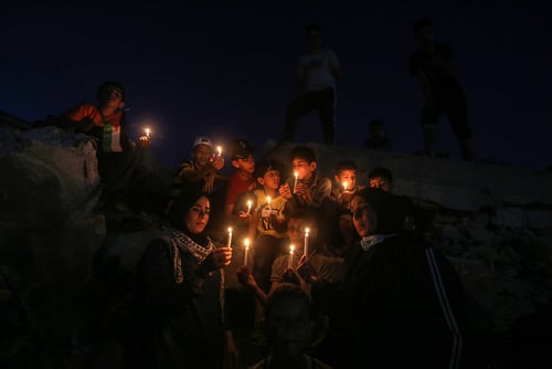 A group of Palestinian children and residents holding lit candles during a nighttime gathering or protest near damaged buildings in Rafah, in the southern Gaza Strip, on May 25, 2021. A group of Palestinian children and residents holding lit candles during a nighttime gathering or protest near damaged buildings in Rafah, in the southern Gaza Strip, on May 25, 2021.