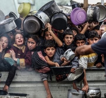 Displaced Palestinian children and residents holding pots and pans while waiting to receive food distribution from a charity kitchen or aid truck during the humanitarian crisis in the Gaza Strip.