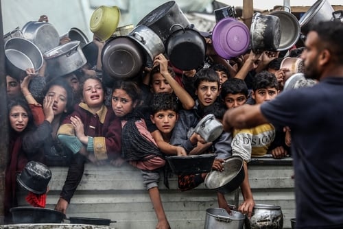 Displaced Palestinian children and residents holding pots and pans while waiting to receive food distribution from a charity kitchen or aid truck during the humanitarian crisis in the Gaza Strip. Displaced Palestinian children and residents holding pots and pans while waiting to receive food distribution from a charity kitchen or aid truck during the humanitarian crisis in the Gaza Strip.