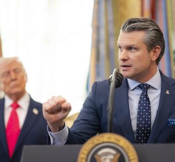 U.S. Defense Secretary Pete Hegseth speaking at a podium with President Donald Trump standing in the background.