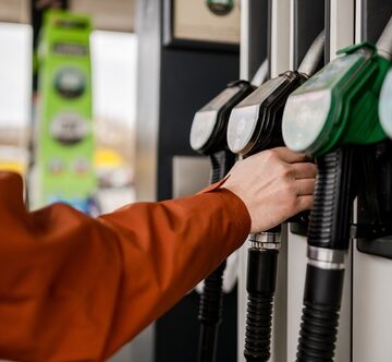 Image of a person holding a fuel pump nozzle at a gas station to refuel a vehicle. Image of a person holding a fuel pump nozzle at a gas station to refuel a vehicle.