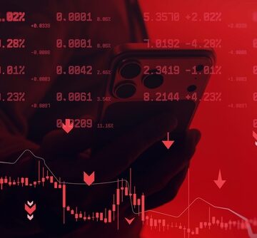 A hand holding a smartphone against a red background filled with downward-trending charts and negative data.