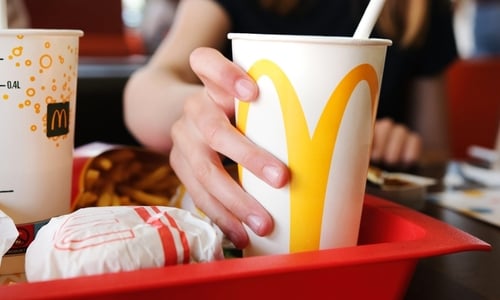 A classic fast-food meal set on a red plastic tray at McDonald's, featuring a wrapped burger, a carton of french fries, and a chilled beverage cup marked with the iconic golden arches. A classic fast-food meal set on a red plastic tray at McDonald's, featuring a wrapped burger, a carton of french fries, and a chilled beverage cup marked with the iconic golden arches.