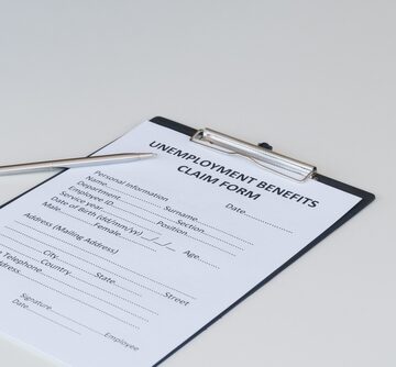 An unemployment benefits claim form clipped to a black clipboard with a silver pen resting beside it.