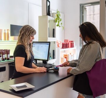 A customer makes a contactless payment at a salon reception desk. A customer makes a contactless payment at a salon reception desk.