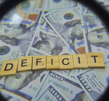 Magnified view of the word "DEFICIT" right over a pile of cash.