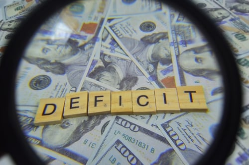 Magnified view of the word "DEFICIT" right over a pile of cash. Magnified view of the word "DEFICIT" right over a pile of cash.