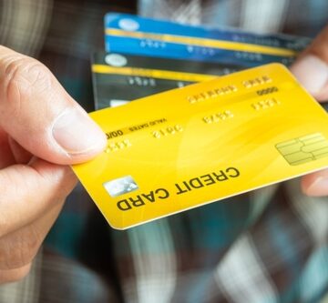A person holding several generic plastic credit cards, with a prominent yellow card featuring a gold chip and the words "CREDIT CARD" in the foreground.