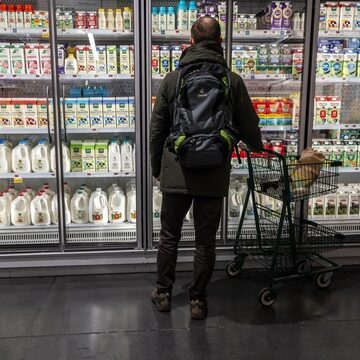 Image of a man wearing a large backpack while shopping for dairy products in a supermarket.