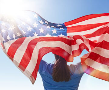 Patriotic,Holiday.,Happy,Young,Woman,With,American,Flag.,Usa,Celebrate AMERICAN DREAM IS BEING REPLACED BY THE ‘GREAT POSTPONEMENT,’ PROFESSOR SAYS