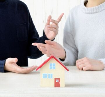 A couple gesturing about real estate decisions or property planning over a small model house.