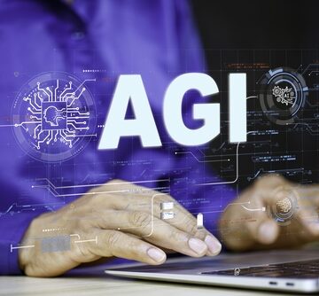 A man at a laptop with a virtual image of the letters "AGI" which stands for Artificial General Intelligence. A man at a laptop with a virtual image of the letters "AGI" which stands for Artificial General Intelligence.