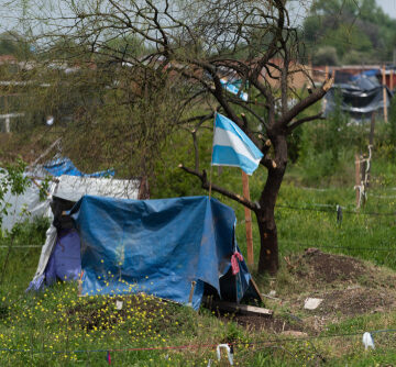 An informal housing or land occupation site in Guernica, Argentina, featuring an Argentine flag flying over a makeshift shelter. An informal housing or land occupation site in Guernica, Argentina, featuring an Argentine flag flying over a makeshift shelter.