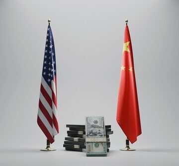 The flags of the United States and China stand on opposite sides of a stack of U.S. dollar bills. The flags of the United States and China stand on opposite sides of a stack of U.S. dollar bills.