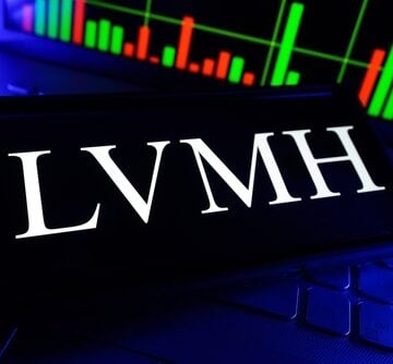 The LVMH (Moët Hennessy Louis Vuitton) logo displayed on a smartphone screen in front of a stock market chart. The LVMH (Moët Hennessy Louis Vuitton) logo displayed on a smartphone screen in front of a stock market chart.