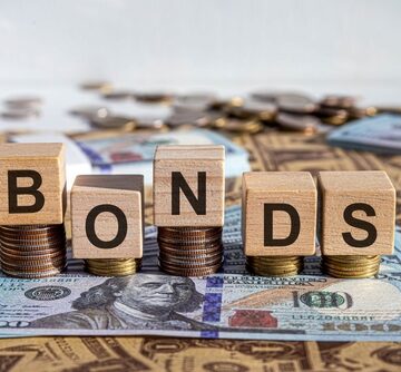 Wooden letter blocks spelling out "BONDS" resting on stacks of coins over US dollar bills.