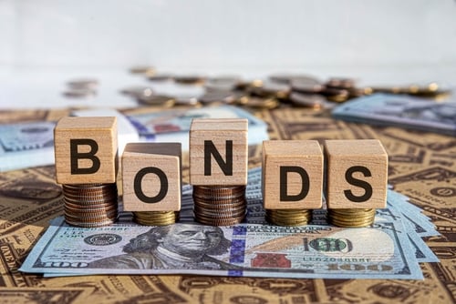 Wooden letter blocks spelling out "BONDS" resting on stacks of coins over US dollar bills.