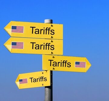 Yellow directional road signs with the word "Tariffs" and U.S. flags pointing in various ways. Yellow directional road signs with the word "Tariffs" and U.S. flags pointing in various ways.