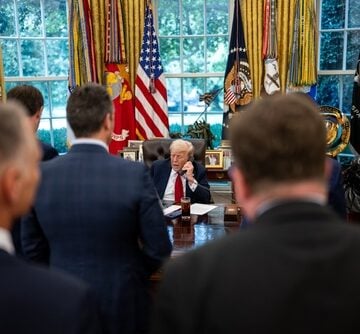 U.S. President Donald Trump seated at the Resolute Desk in the Oval Office while on a phone call, surrounded by staff and officials. U.S. President Donald Trump seated at the Resolute Desk in the Oval Office while on a phone call, surrounded by staff and officials.